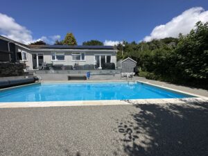 this image shows grey resin surrounding a pool with a one-floor house behind it