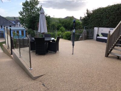 resin patio with furniture, glass fence and slope leading up to it